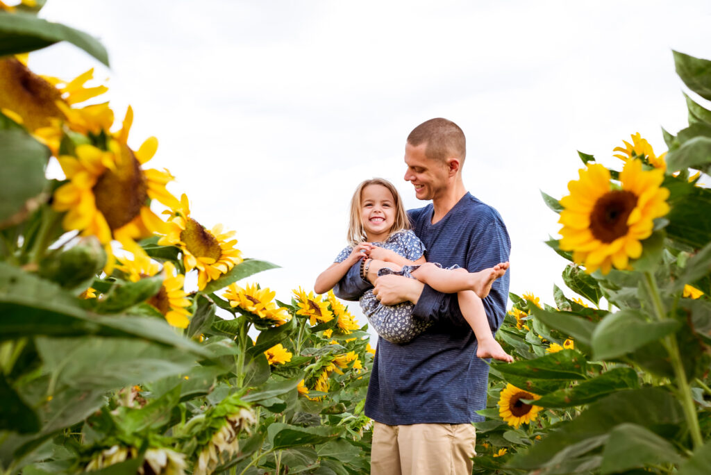 daughter held by her dad in flower field during the season for apple picking in Phoenix AZ