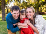 parents of young daughter laughing and smiling as they tickle her and squeeze close together in an orchard for apple picking in Phoenix AZ
