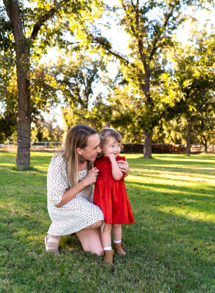mother kneeling down to snuggle her daughter while in an orchard for apple picking in Phoenix AZ