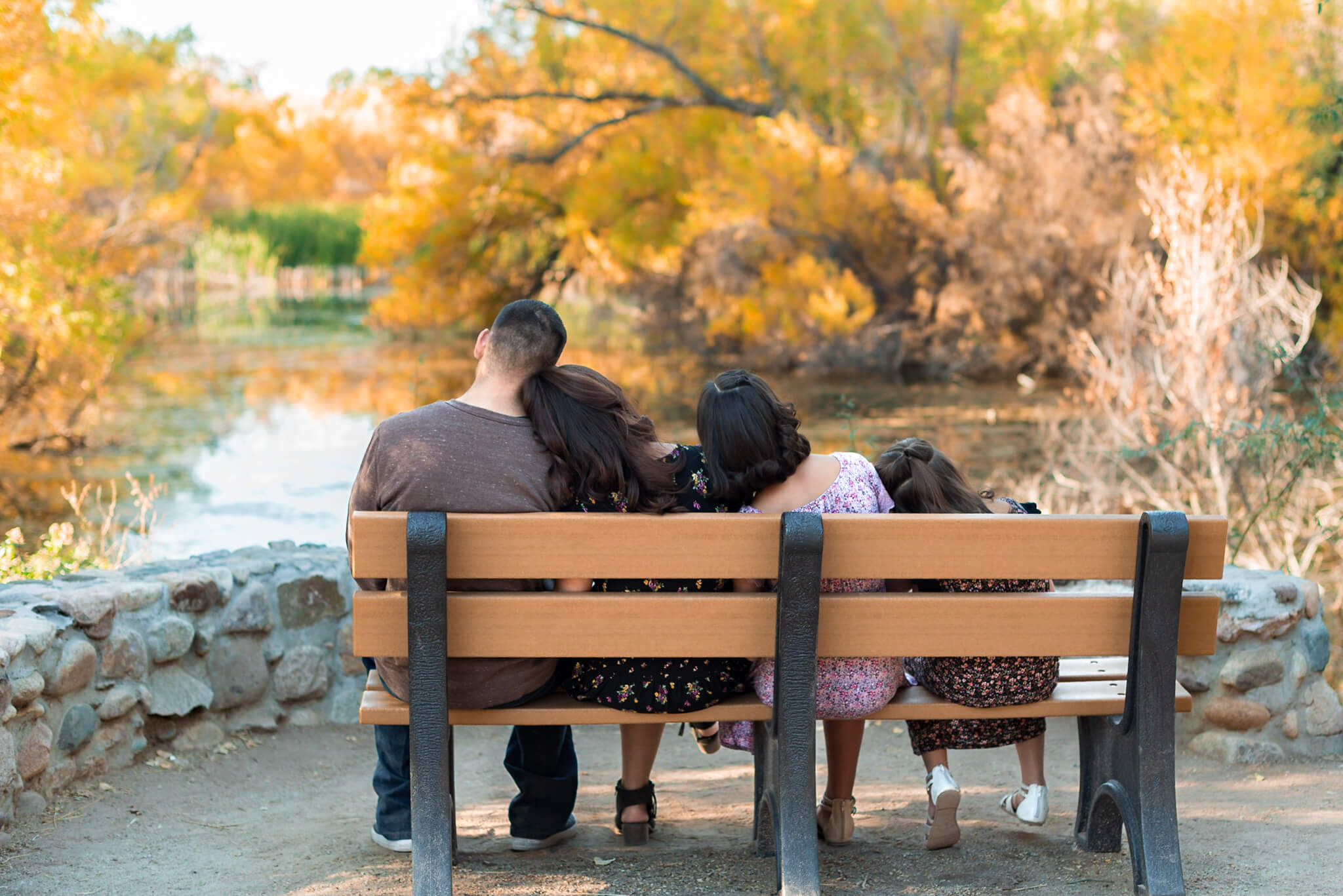 family sitting on a bench enjoying a waterfront view with fall foliage in colors similar to a corn maze in Phoenix, AZ