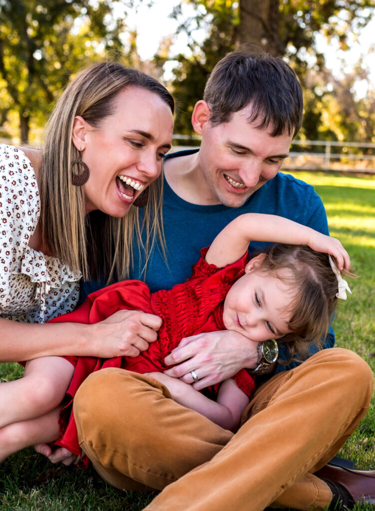 parents sitting in grass near a corn maze in phoenix with their daughter