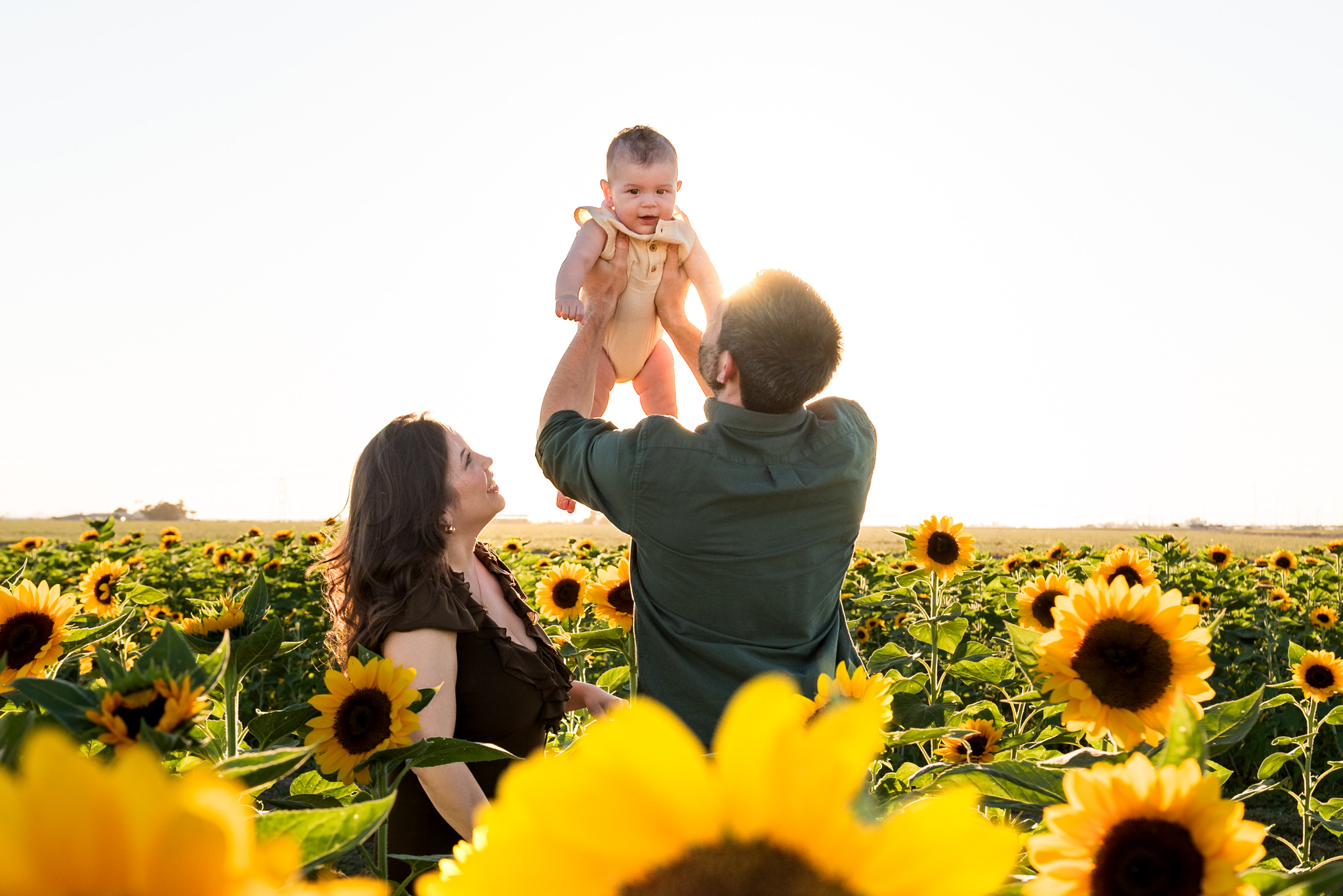 dad holding baby next to wife in sunflower field at fall festivals in phoenix, AZ
