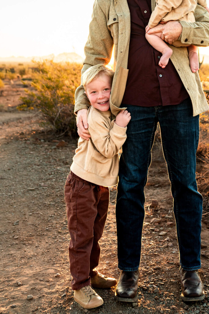 sweet portrait of son hugging dad's leg to stay warm near christmas at a tree farm