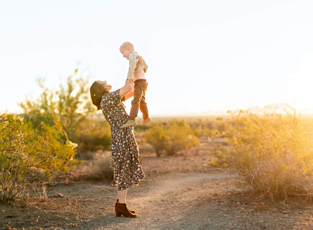 Mom near a tree farm at Christmas, lifting her son into the air during an Arizona sunrise